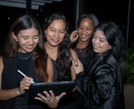 four women are smiling while using a tablet