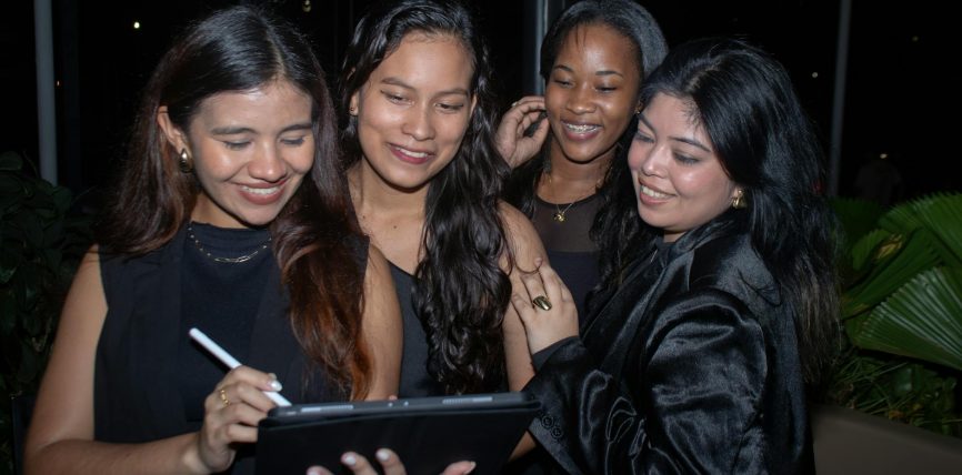 four women are smiling while using a tablet