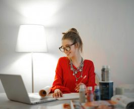 woman in red long sleeve shirt looking at her laptop