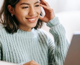 hispanic woman working remotely on laptop near notepad in apartment