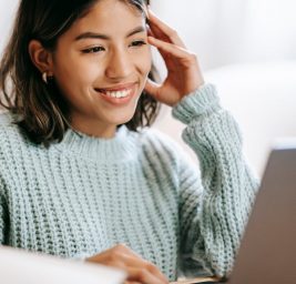 hispanic woman working remotely on laptop near notepad in apartment